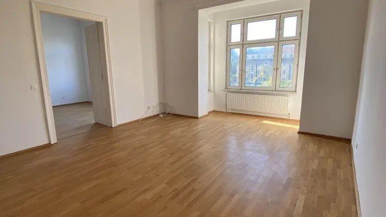 Helles Wohnzimmer mit klassischem Parkettboden und großen Fenstern, das viel Tageslicht hereinlässt.