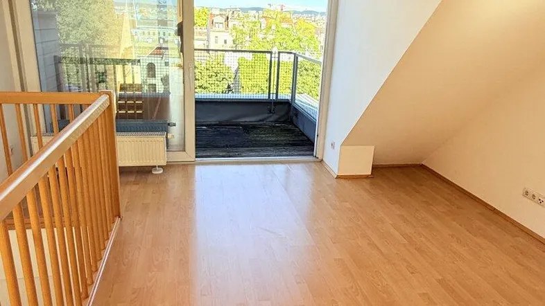 Heller Wohnbereich mit Laminatboden, Dachschrägen und Zugang zu einer Dachterrasse mit Stadtblick.