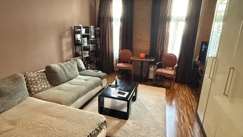 Helles Wohnzimmer mit Parkettboden, bequemer Eckcouch und dekorativen Vorhängen an den Fenstern.