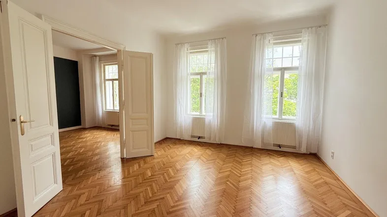 Helles Wohnzimmer mit Fischgrätparkettboden und hohen Flügeltüren, das viel Tageslicht bietet.