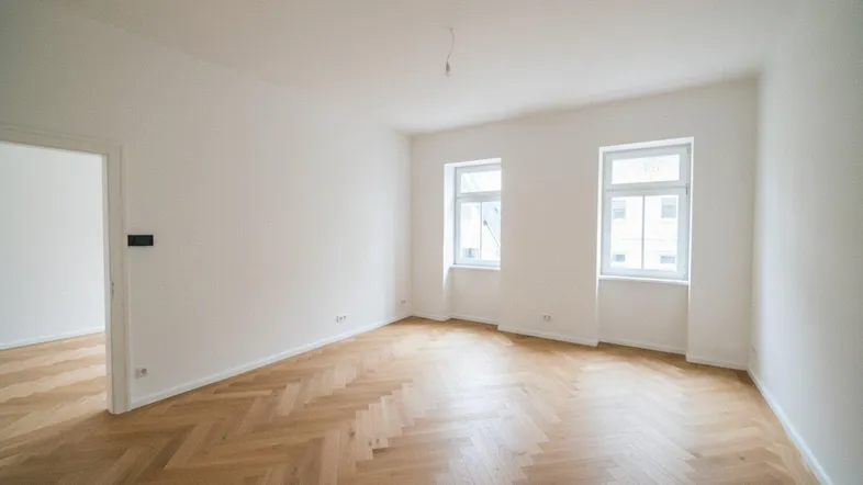 Heller, leerer Raum mit elegantem Fischgrätparkett und zwei Fenstern, ideal für Wohnzwecke.