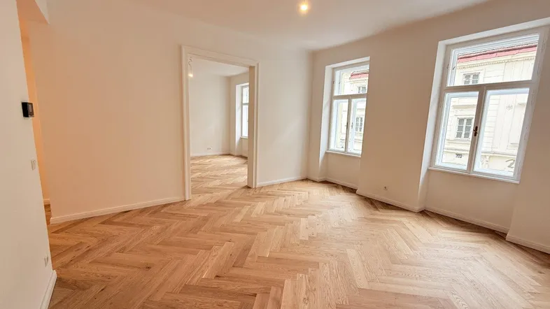 Helles Zimmer mit Fischgrätparkett und hohen Fenstern, bereit zur individuellen Gestaltung.