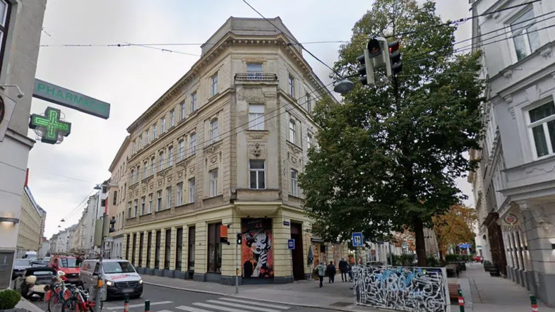 Historisches Eckgebäude an einer belebten Straße mit traditioneller Architektur und großen Fenstern im Stadtzentrum.