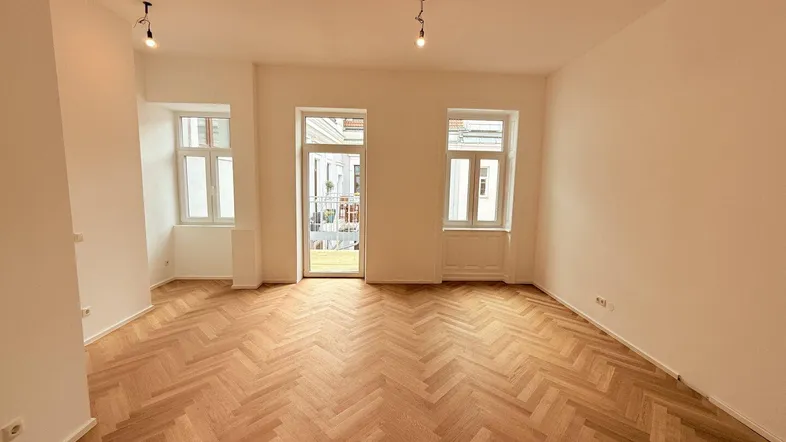 Helles Wohnzimmer mit Fischgrätparkett, hohen Decken und Zugang zu einem kleinen Balkon.