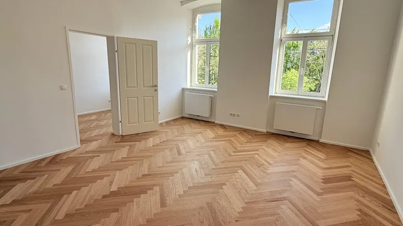 Helles Wohnzimmer mit neu verlegtem Fischgrätparkett und zwei großen Fenstern mit Blick ins Grüne.