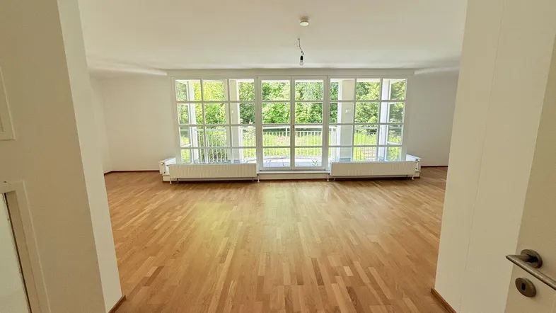 Helles Wohnzimmer mit Parkettboden, großen Fenstern und einem schönen Blick ins Grüne.