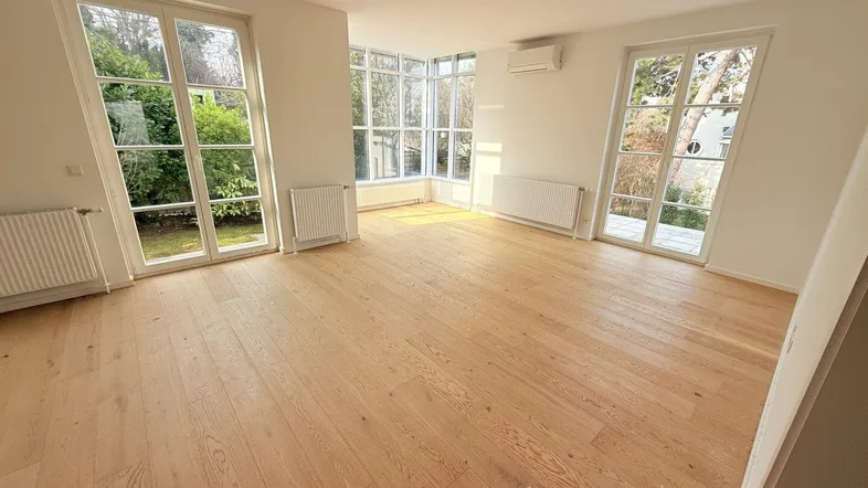 Helles Wohnzimmer mit großen Fenstern, Holzboden und Blick ins Grüne.