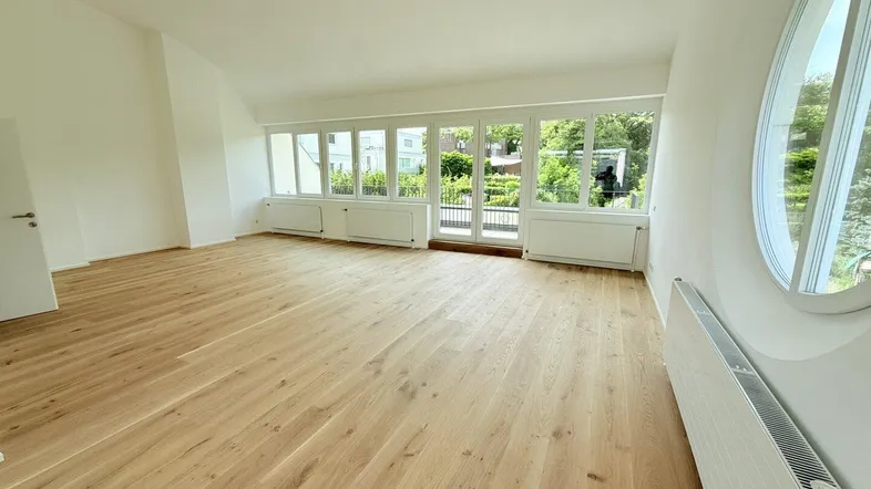 Helles Wohnzimmer mit Eichenparkett, großen Fenstern und einem markanten runden Fenster.