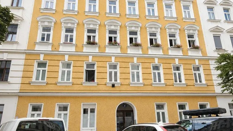 Klassisches Mehrfamilienhaus mit gelber Fassade, vielen Fenstern und Parkplätzen davor.
