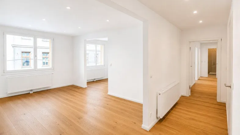 Helles, frisch renoviertes Wohnzimmer mit neuem Parkettboden und großen Fenstern.