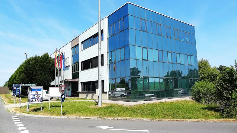 Modernes Bürogebäude mit Glasfassade und umliegender Grünfläche unter blauem Himmel.