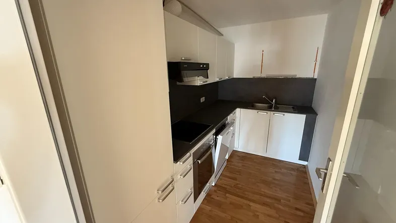 Moderne Einbauküche mit weißen Schränken, dunkler Arbeitsplatte und Holzboden.