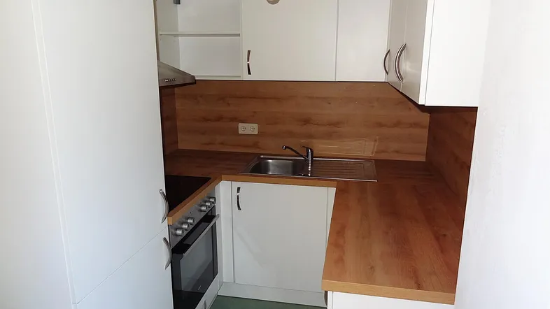 Kleine Küche mit weißen Schränken, Holz-Arbeitsplatten, Spüle und integriertem Herd.