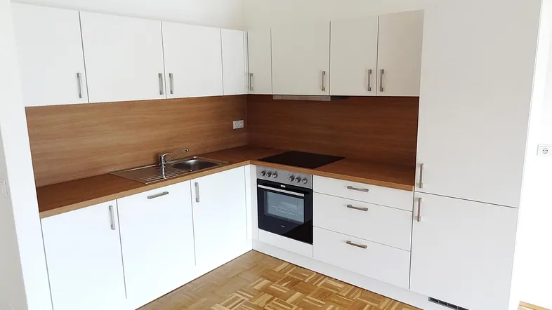 Moderne Einbauküche mit weißen Schränken, Holzarbeitsplatte, Induktionskochfeld und Parkettboden.