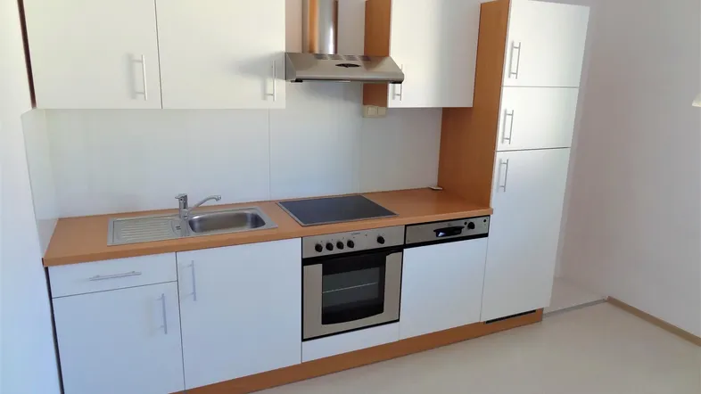 Funktionale Einbauküche mit weißen Schränken, Holztheke und integrierten Geräten.