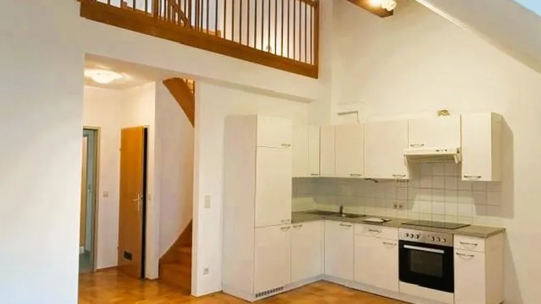 Helle Küche mit weißen Schränken, integriertem Backofen und Blick auf die Holztreppe zum Loft.