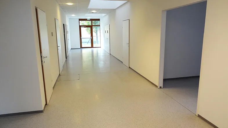 Langer, heller Flur mit mehreren Türen und einem Fenster am Ende, das Tageslicht hereinlässt.