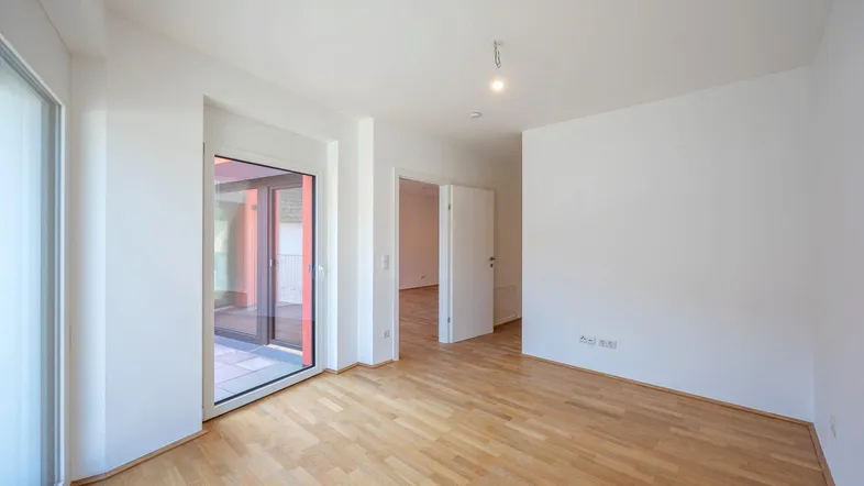 Helles Zimmer mit Parkettboden und Zugang zu einem sonnigen Außenbereich.