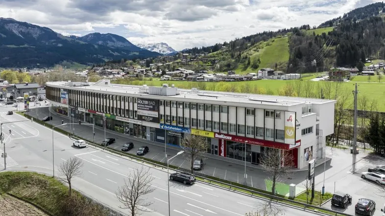Luftaufnahme eines modernen Geschäftsgebäudes mit Geschäften und Büros, umgeben von einer malerischen Berglandschaft.