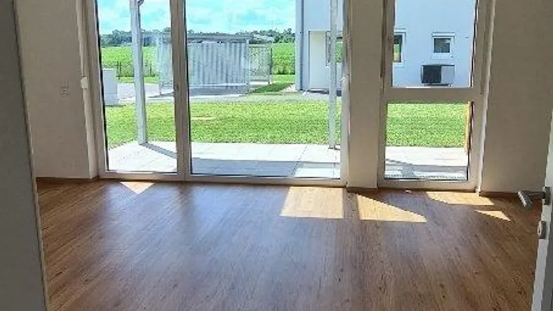 Helles Wohnzimmer mit Holzboden und großen Schiebetüren, die Zugang zum Garten bieten.