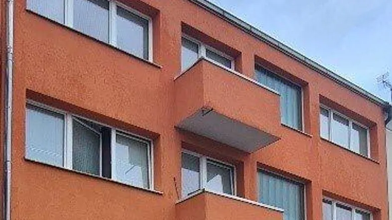 Gebäudefassade eines Mehrfamilienhauses mit orangefarbenem Putz und kleinen Balkonen.