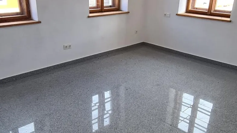 Helles, leeres Zimmer mit drei Holzfenstern und glänzendem Granitboden, bereit für die individuelle Gestaltung.