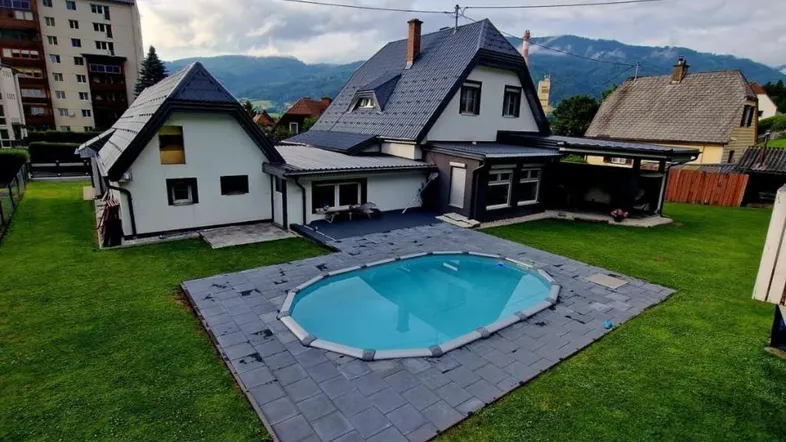 Haus mit Garten, ovalem Pool und Bergblick unter bewölktem Himmel.