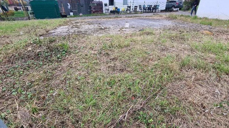 Ungenutztes Grundstück mit Gras und Blick auf Nachbargebäude in ländlicher Umgebung.