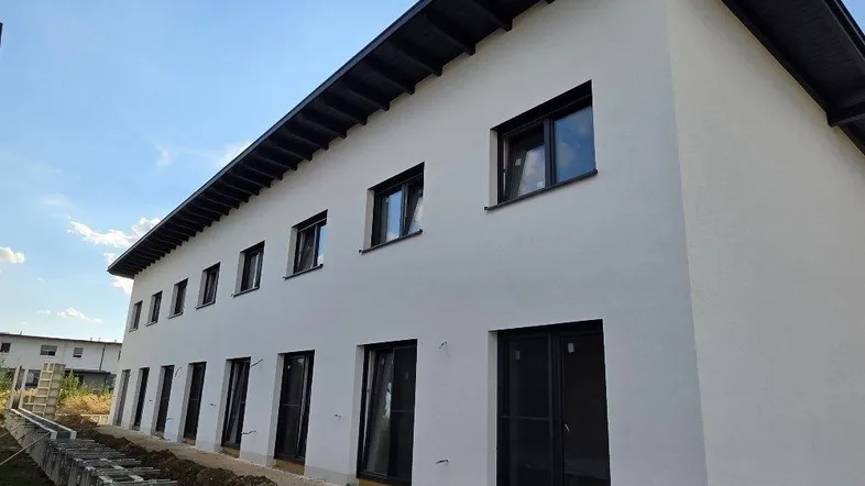 Ansicht der modernen Gebäudefassade eines Neubaus mit weißen Wänden und dunklem Satteldach.