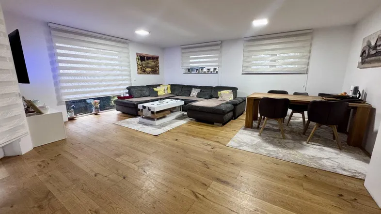 Geräumiger Wohn-Essbereich mit dunklem Ecksofa, Esstisch und hellem Holzfußboden.