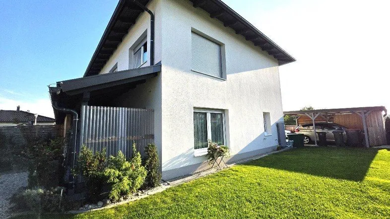 Weißes Einfamilienhaus mit Satteldach, gepflegtem Rasen und Carport im Gartenbereich.