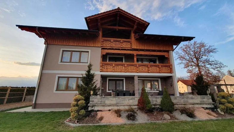 Traditionelles Haus mit Holzfassade und mehreren Balkonen, umgeben von einem gepflegten Garten.