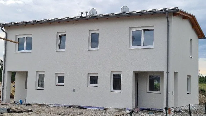 Ansicht der modernen Neubaufassade mit hellgrauem Putz und Satteldach unter bewölktem Himmel.