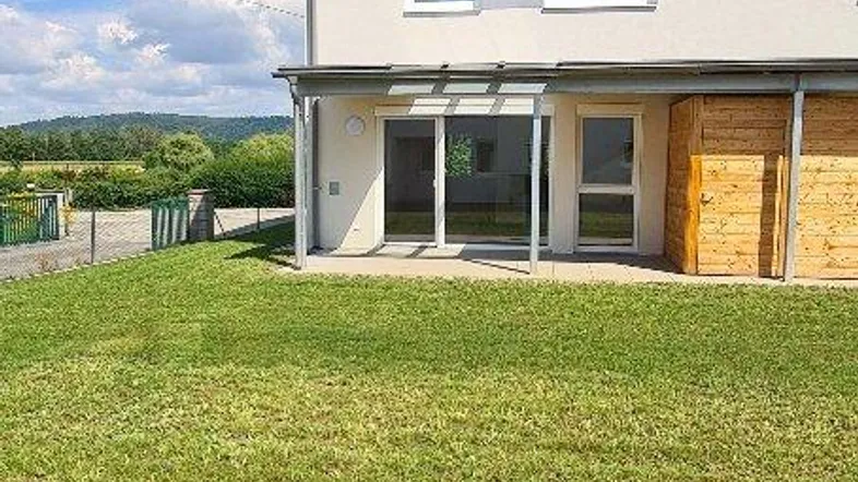 Modernes Reihenhaus mit großer Rasenfläche und Blick ins Grüne unter blauem Himmel.