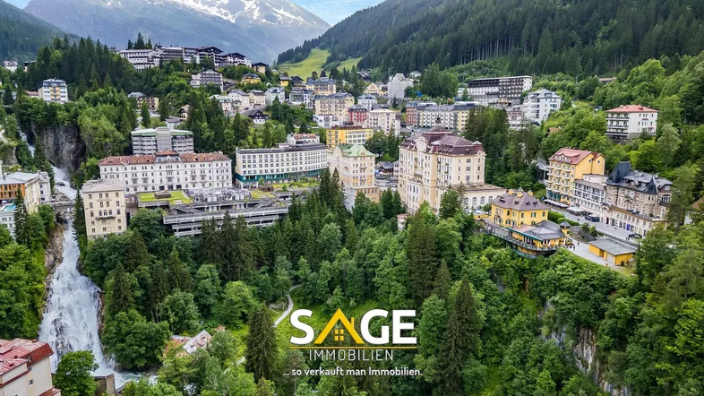 Luftaufnahme einer malerischen Stadt in einem Tal mit Bergen und einem beeindruckenden Wasserfall.