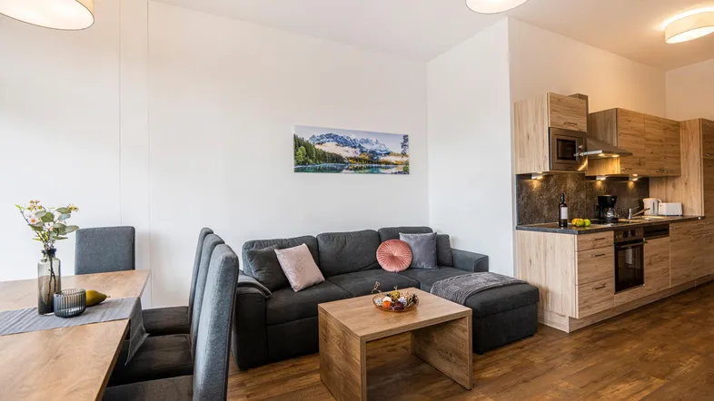 Moderner offener Wohn-Essbereich mit integrierter Küche, Holzfußboden und Bergbild an der Wand.