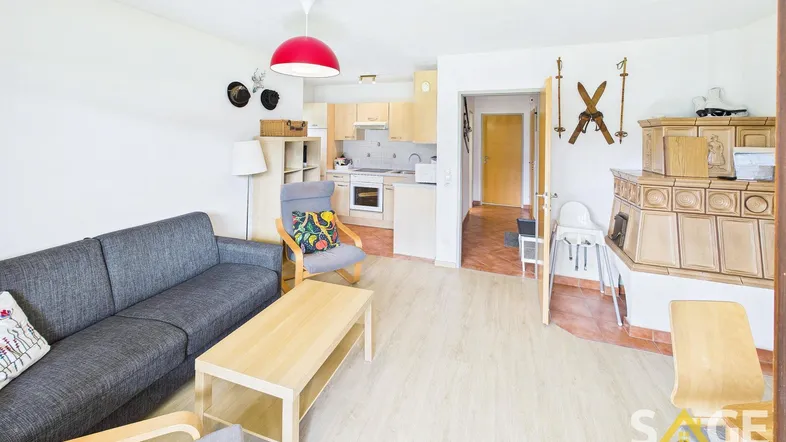 Gemütlicher Wohnbereich mit Sofa, Kachelofen und integrierter Küchenzeile in hellem Ambiente.