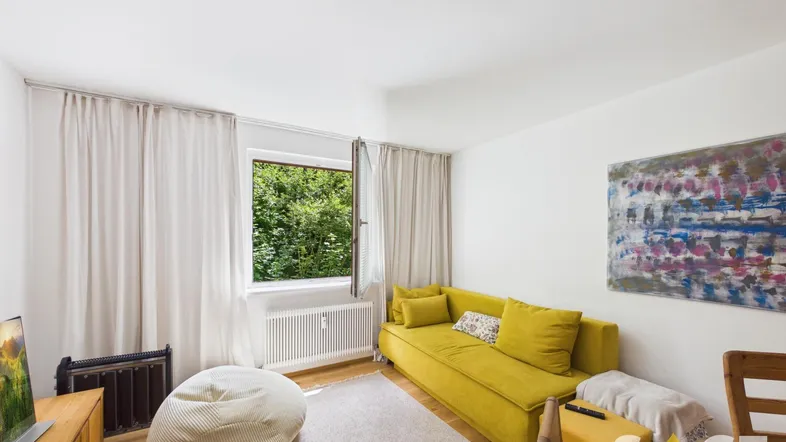 Helles Wohnzimmer mit gelbem Sofa, Holzboden und Blick ins Grüne durch das Fenster.
