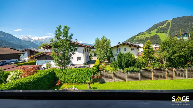 Panoramablick auf die umliegende Berglandschaft mit grünen Hügeln und Wohnhäusern unter blauem Himmel.