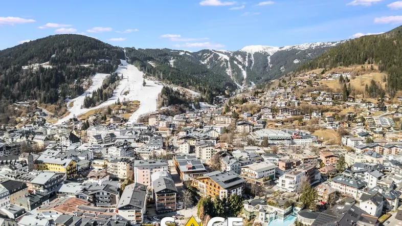 Panoramablick auf eine malerische Bergstadt mit schneebedeckten Pisten und umliegenden Bergen unter blauem Himmel.