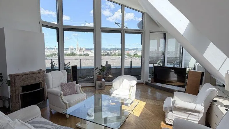 Helles Wohnzimmer mit großen Fenstern, Dachschrägen und Blick auf die Stadt.