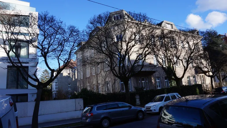 Historisches Gebäude mit klassischer Architektur und Bäumen an einer städtischen Straße.