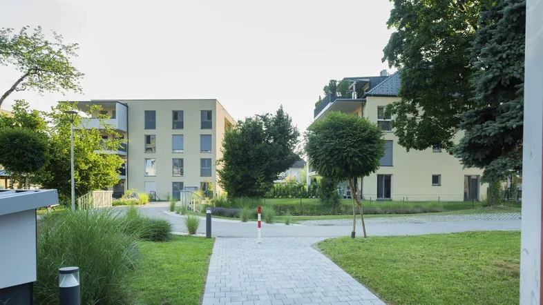 Moderne Wohngebäude in einer gepflegten Grünanlage mit Gehwegen und Bäumen.