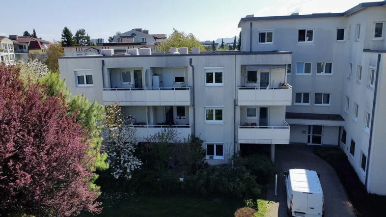 Mehrfamilienhaus mit mehreren Balkonen und gepflegter Grünanlage unter blauem Himmel im Frühling.