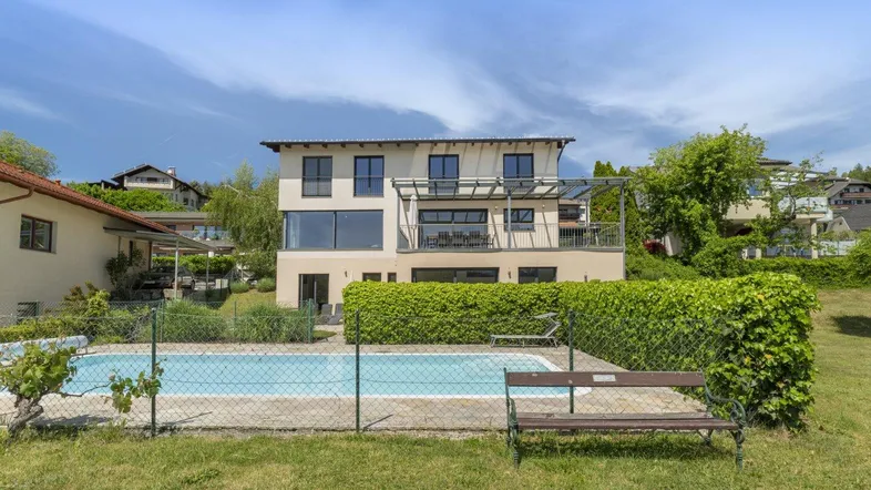 Modernes Haus mit großem Pool und gepflegter Hecke im Gartenbereich unter blauem Himmel.