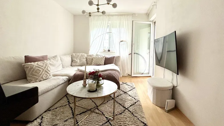 Helles Wohnzimmer mit beigem Ecksofa, modernem Couchtisch und Zugang zum Balkon.