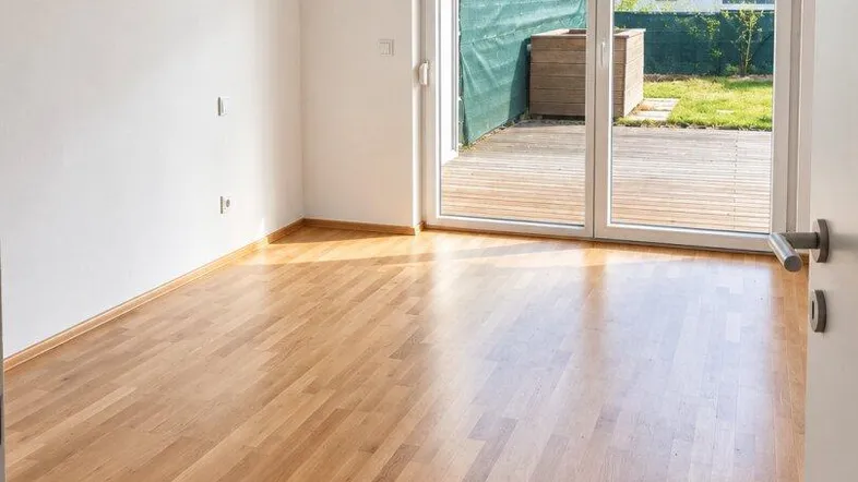 Heller Raum mit Holzboden und großer Glasschiebetür, die Zugang zu einer Terrasse bietet.