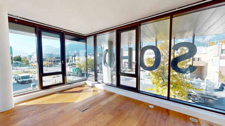 Heller Innenraum mit großen Fenstern, Holzboden und Blick auf die Stadt und Berge.