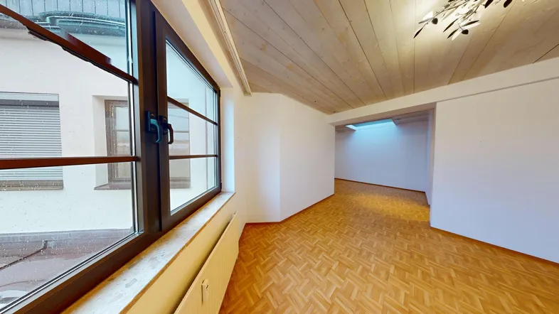 Heller Wohnbereich im Dachgeschoss mit Holzbalkendecke, Parkettboden und großem Fenster.