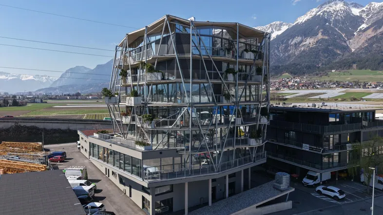 Modernes Gebäude mit einzigartiger Glasfassade und geometrischer Struktur, umgeben von Bergen und einer städtischen Landschaft.